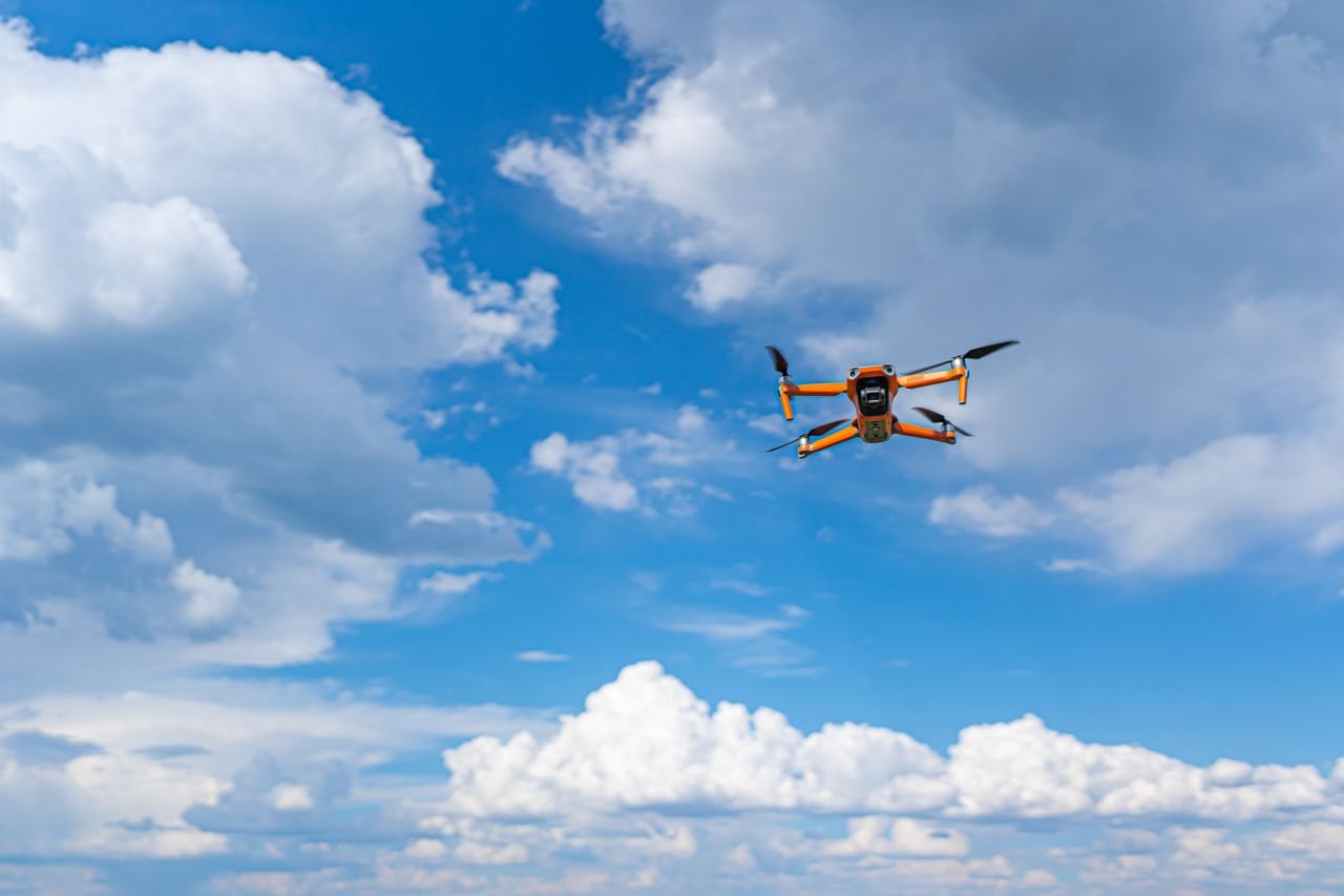 Drone flying mid-air against a vibrant blue sky with fluffy clouds, showcasing modern technology and aerial photography.